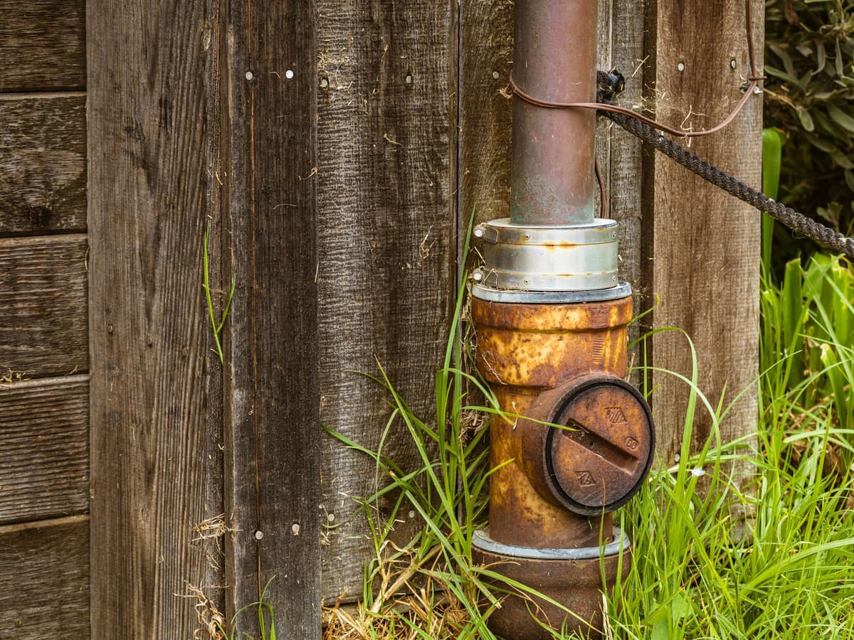 Sewer cleanout cap beside a wood-sided house